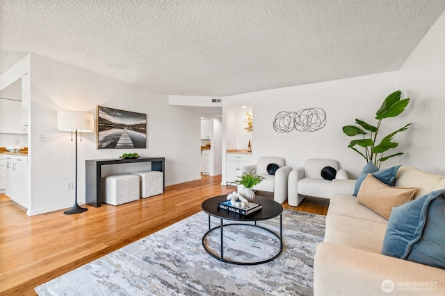 living room featuring light wood-style flooring, a textured ceiling, and visible vents