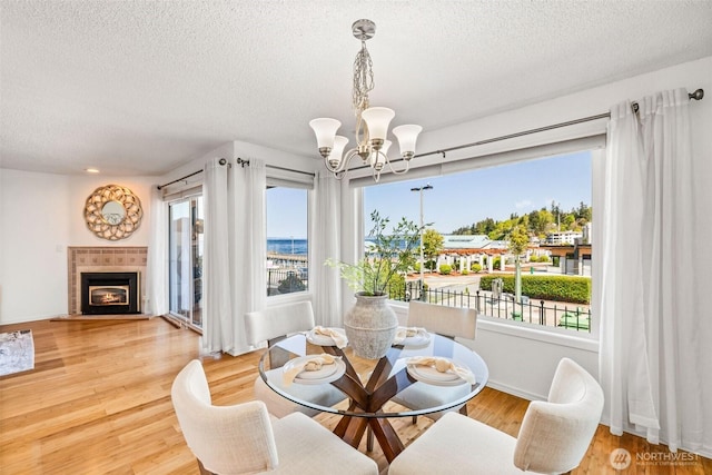 dining room with a tiled fireplace, wood finished floors, a textured ceiling, and a chandelier