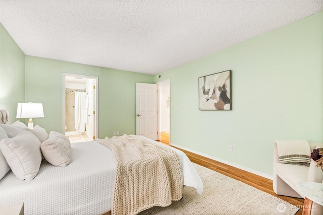 bedroom with baseboards, a textured ceiling, ensuite bathroom, and wood finished floors