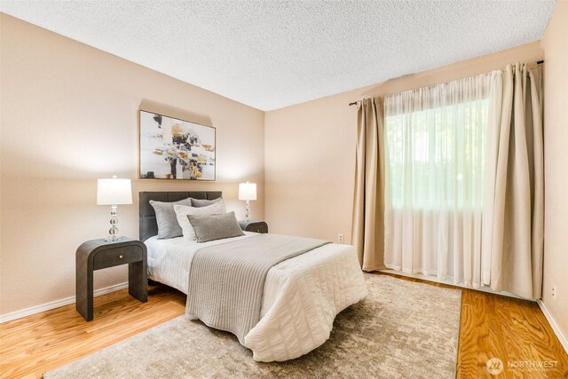 bedroom featuring a textured ceiling, baseboards, and wood finished floors