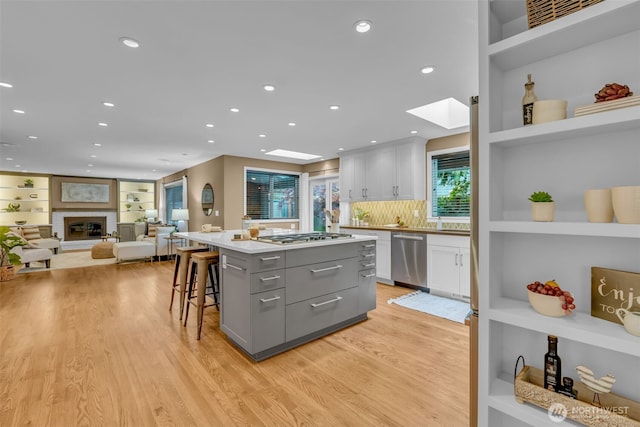 kitchen with a kitchen island, a skylight, gray cabinetry, light wood-style floors, and stainless steel appliances