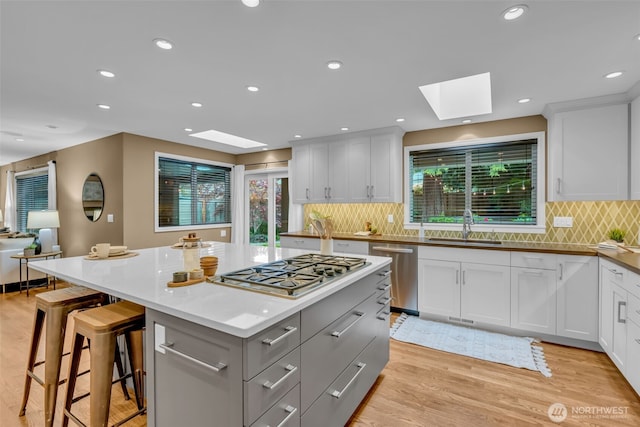 kitchen with a sink, stainless steel appliances, a kitchen island, a skylight, and gray cabinetry