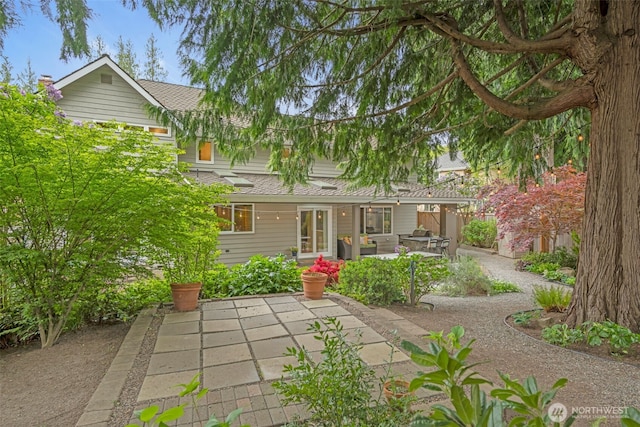 back of property with roof with shingles and a patio area