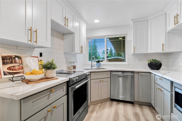 kitchen with a sink, stainless steel appliances, light wood-type flooring, gray cabinets, and light stone countertops