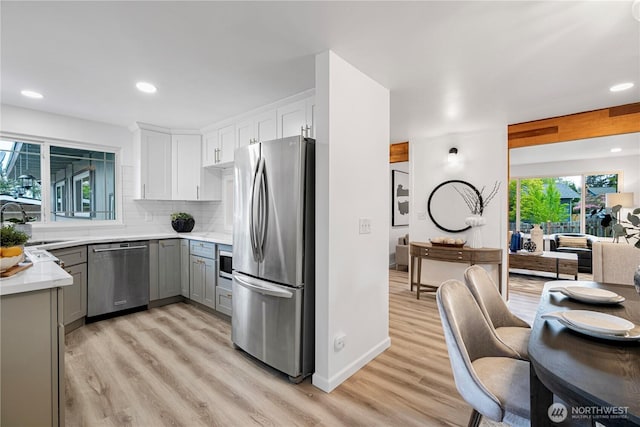 kitchen with gray cabinetry, appliances with stainless steel finishes, a sink, and light wood-style floors