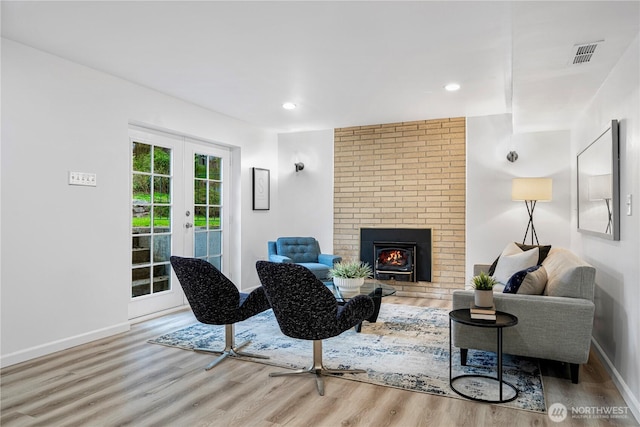 living room featuring wood finished floors, french doors, a fireplace, visible vents, and baseboards
