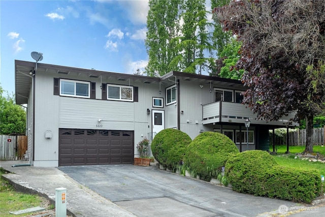 raised ranch featuring an attached garage, concrete driveway, fence, and a balcony
