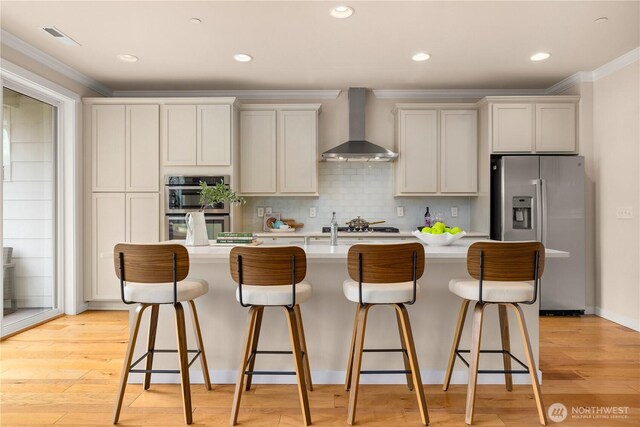 kitchen with wall chimney exhaust hood, appliances with stainless steel finishes, ornamental molding, light countertops, and a kitchen bar