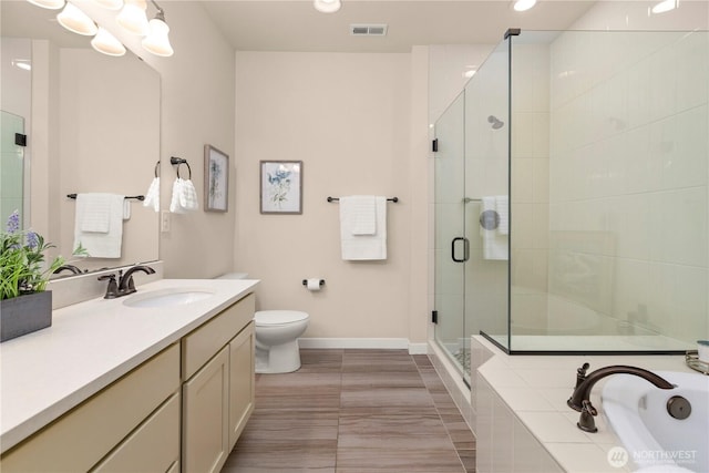 bathroom with a shower stall, baseboards, vanity, toilet, and tiled bath
