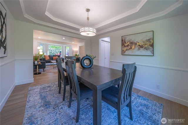 dining space with a tray ceiling, wood finished floors, crown molding, and baseboards