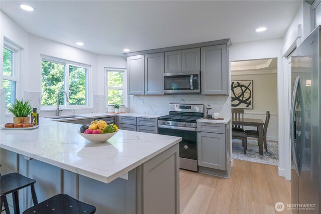 kitchen with appliances with stainless steel finishes, gray cabinetry, a sink, light wood-style floors, and a kitchen breakfast bar