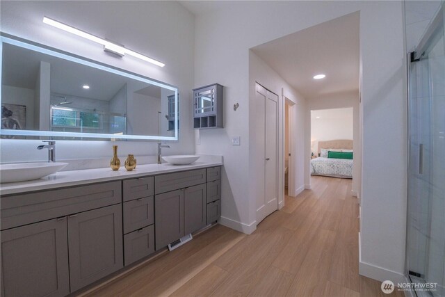 ensuite bathroom with a stall shower, baseboards, wood finished floors, and double vanity