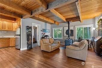 living area featuring a wood stove, beam ceiling, wood finished floors, wooden ceiling, and baseboards