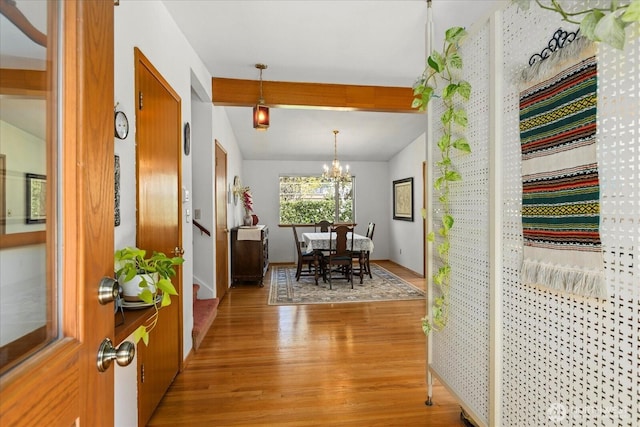 hallway with beam ceiling, a notable chandelier, and light wood-style flooring