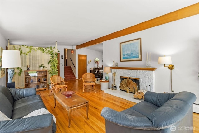 living area featuring a fireplace with raised hearth, stairs, wood finished floors, and beamed ceiling