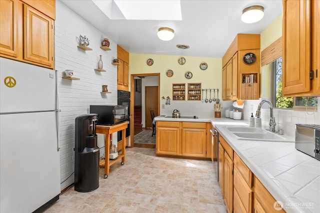 kitchen with tile countertops, tasteful backsplash, a sink, black appliances, and a skylight