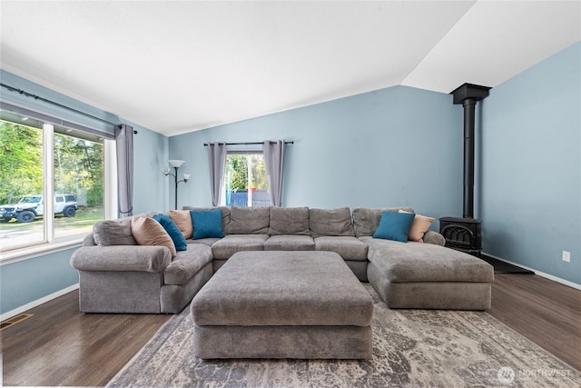 living room with visible vents, a wood stove, vaulted ceiling, wood finished floors, and baseboards
