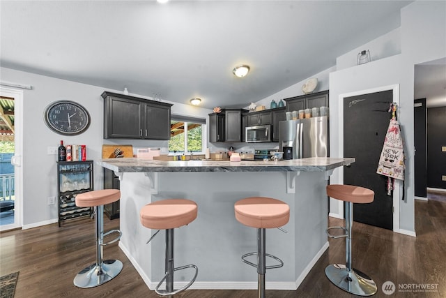 kitchen with a kitchen breakfast bar, a center island, dark wood finished floors, appliances with stainless steel finishes, and vaulted ceiling
