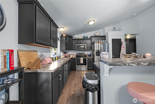 kitchen featuring a kitchen breakfast bar, dark wood-type flooring, a sink, vaulted ceiling, and stainless steel appliances