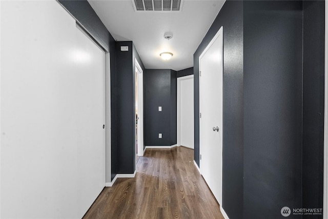 corridor with baseboards, wood finished floors, and visible vents