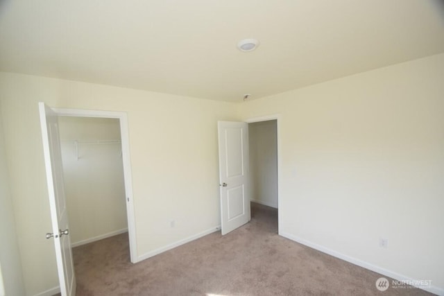 unfurnished bedroom with baseboards, a walk in closet, a closet, and light colored carpet