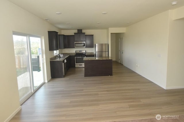 kitchen with appliances with stainless steel finishes, a center island, light wood-type flooring, a sink, and baseboards
