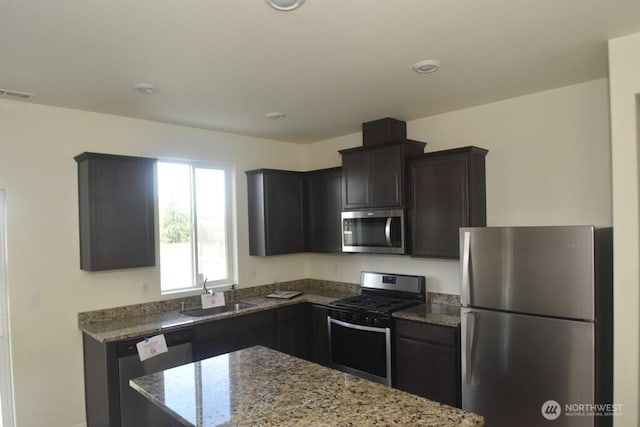 kitchen with appliances with stainless steel finishes, stone counters, a sink, and visible vents