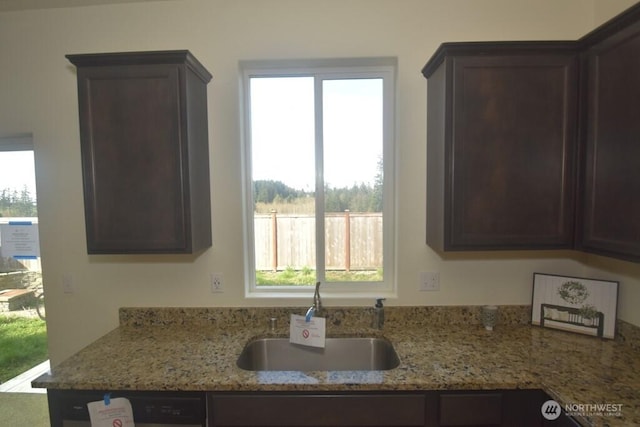 kitchen with light stone counters, a sink, and dark brown cabinets