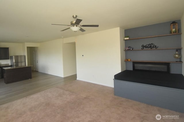 unfurnished living room featuring baseboards, carpet flooring, a glass covered fireplace, and a ceiling fan