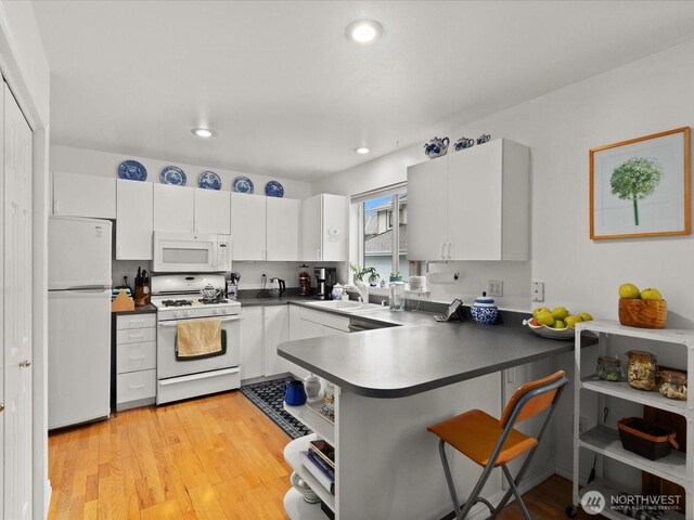 kitchen with white appliances, a peninsula, dark countertops, and white cabinetry