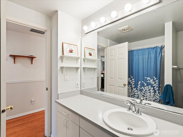 bathroom with vanity, baseboards, wood finished floors, a shower with curtain, and visible vents
