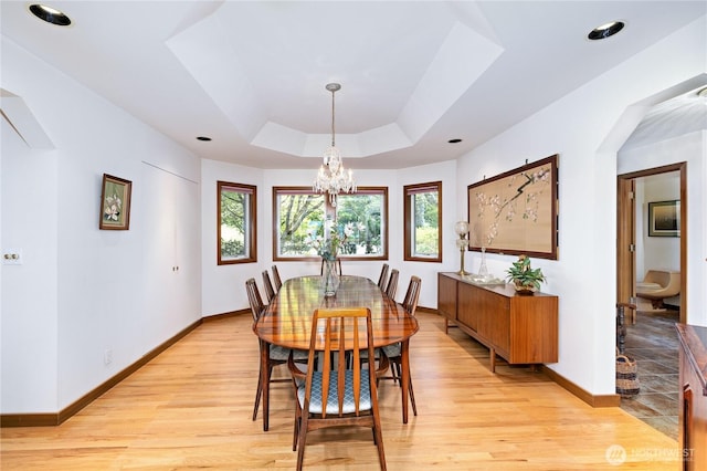 dining area with baseboards, a chandelier, a tray ceiling, and light wood-style floors
