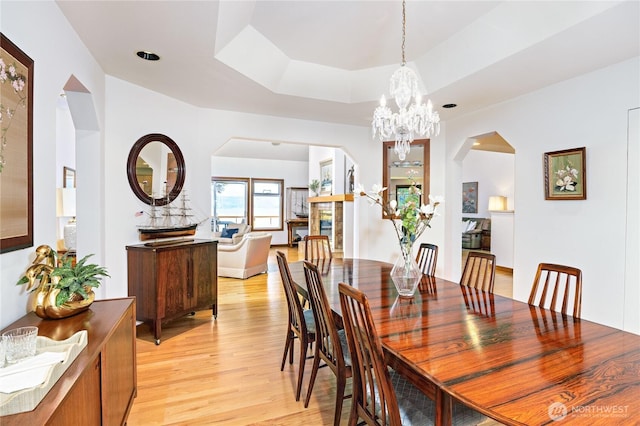dining room featuring an inviting chandelier, arched walkways, light wood-type flooring, and a raised ceiling