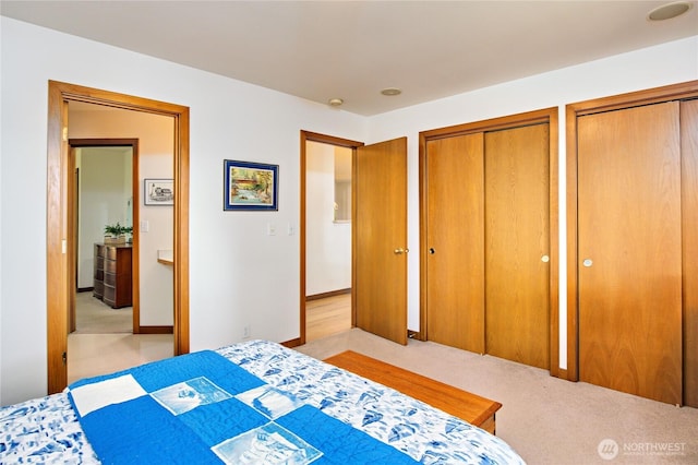 bedroom featuring light colored carpet and multiple closets