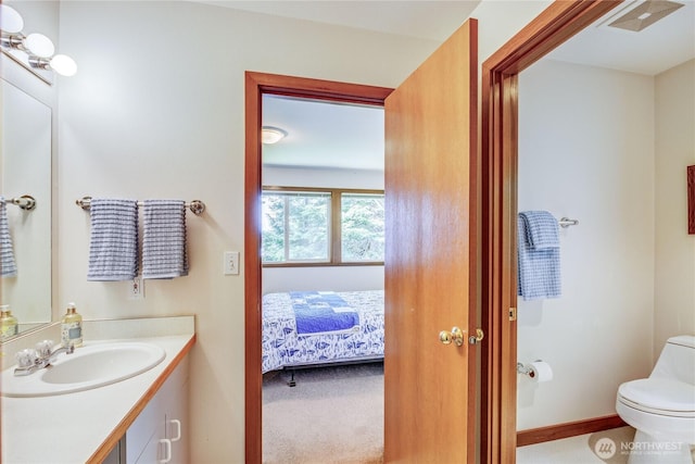 ensuite bathroom with connected bathroom, vanity, toilet, baseboards, and visible vents