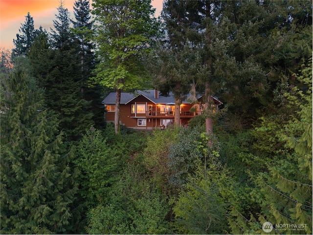 back of house at dusk featuring a view of trees and a chimney