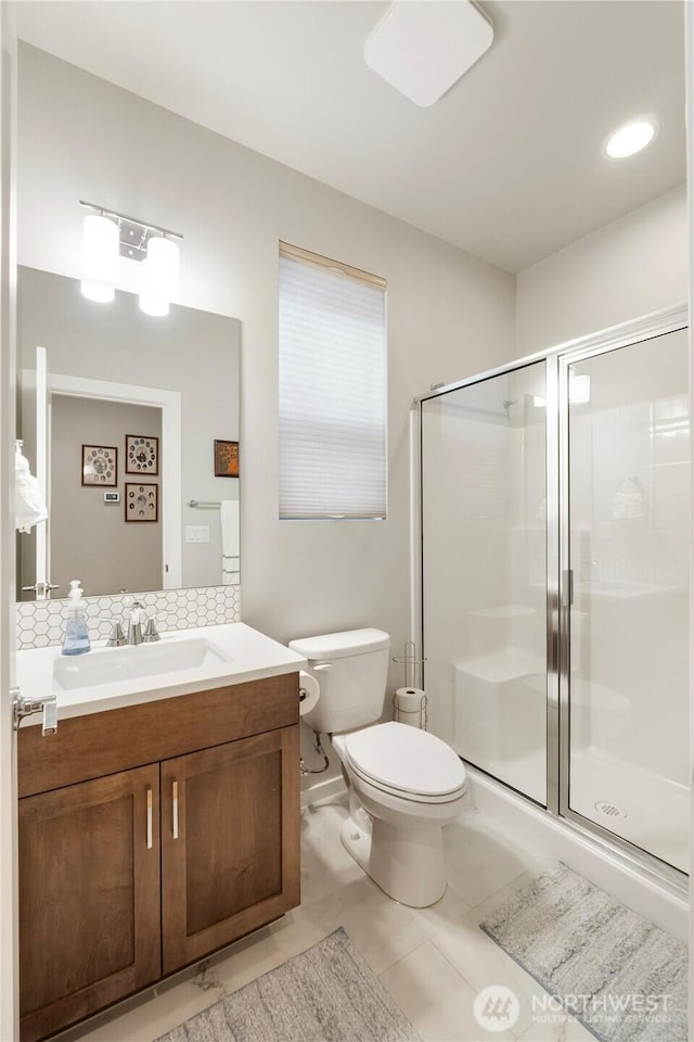 bathroom with backsplash, toilet, a shower stall, and vanity