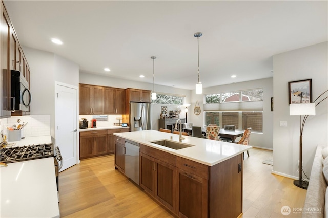 kitchen featuring a sink, a kitchen island with sink, stainless steel appliances, and light wood-style flooring