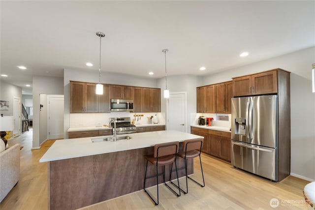 kitchen featuring decorative backsplash, light wood-type flooring, light countertops, a sink, and appliances with stainless steel finishes