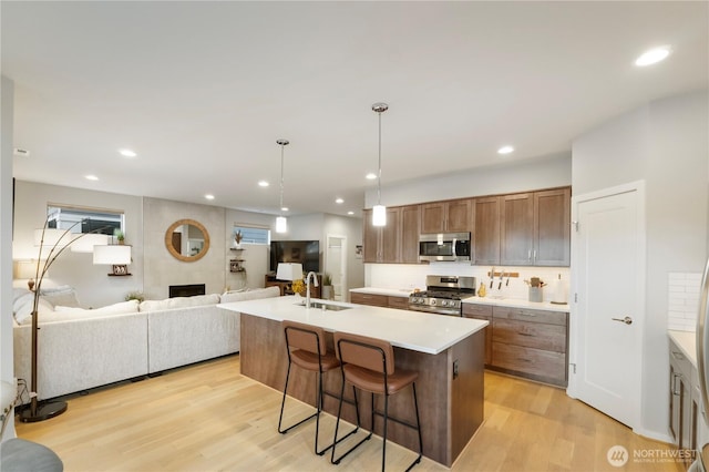 kitchen with appliances with stainless steel finishes, a sink, a fireplace, light countertops, and light wood-style flooring