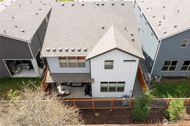 back of property with central air condition unit, board and batten siding, roof with shingles, and fence