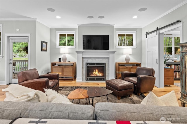 living room with plenty of natural light, crown molding, a barn door, wood finished floors, and a warm lit fireplace