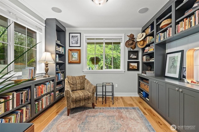 sitting room with baseboards, ornamental molding, light wood-style flooring, and built in shelves
