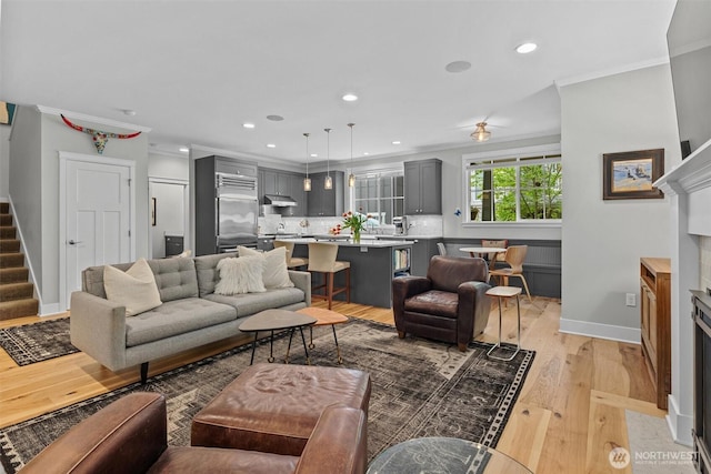 living room featuring crown molding, recessed lighting, baseboards, light wood-type flooring, and stairway