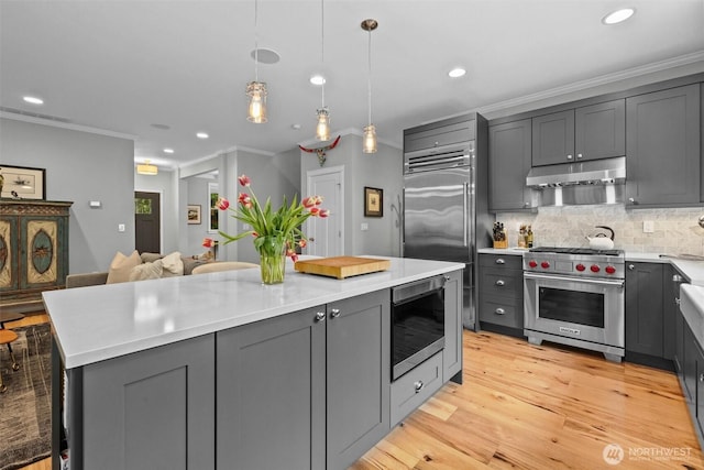 kitchen featuring built in appliances, light countertops, gray cabinets, recessed lighting, and under cabinet range hood