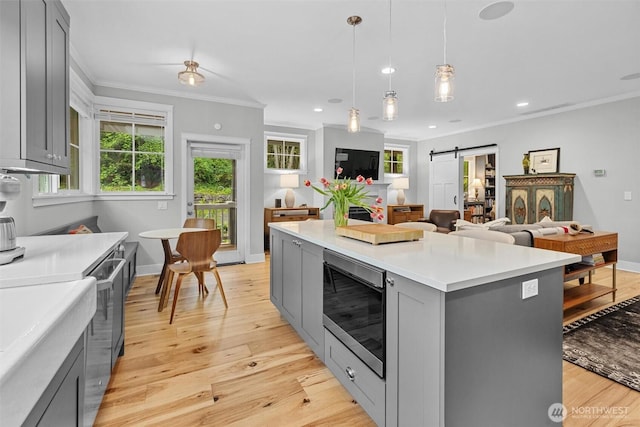 kitchen with crown molding, a barn door, light countertops, stainless steel microwave, and gray cabinetry