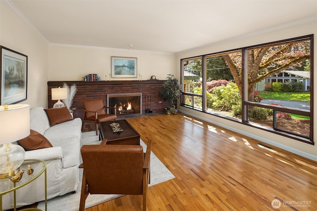 living room featuring crown molding, visible vents, a brick fireplace, wood finished floors, and baseboards