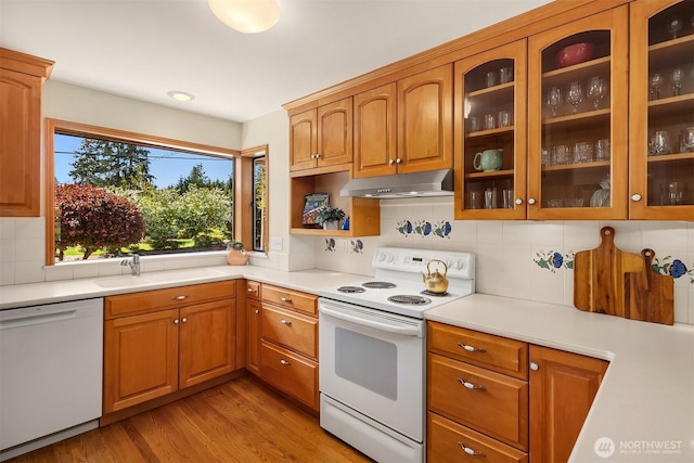 kitchen with a sink, white appliances, light countertops, light wood-style flooring, and under cabinet range hood