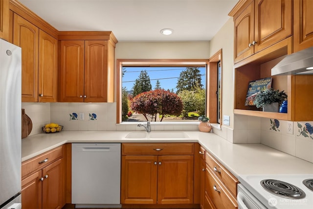 kitchen with white appliances, decorative backsplash, a sink, and light countertops