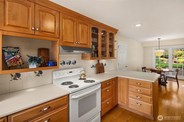 kitchen featuring a peninsula, under cabinet range hood, white range with electric stovetop, brown cabinets, and light wood finished floors